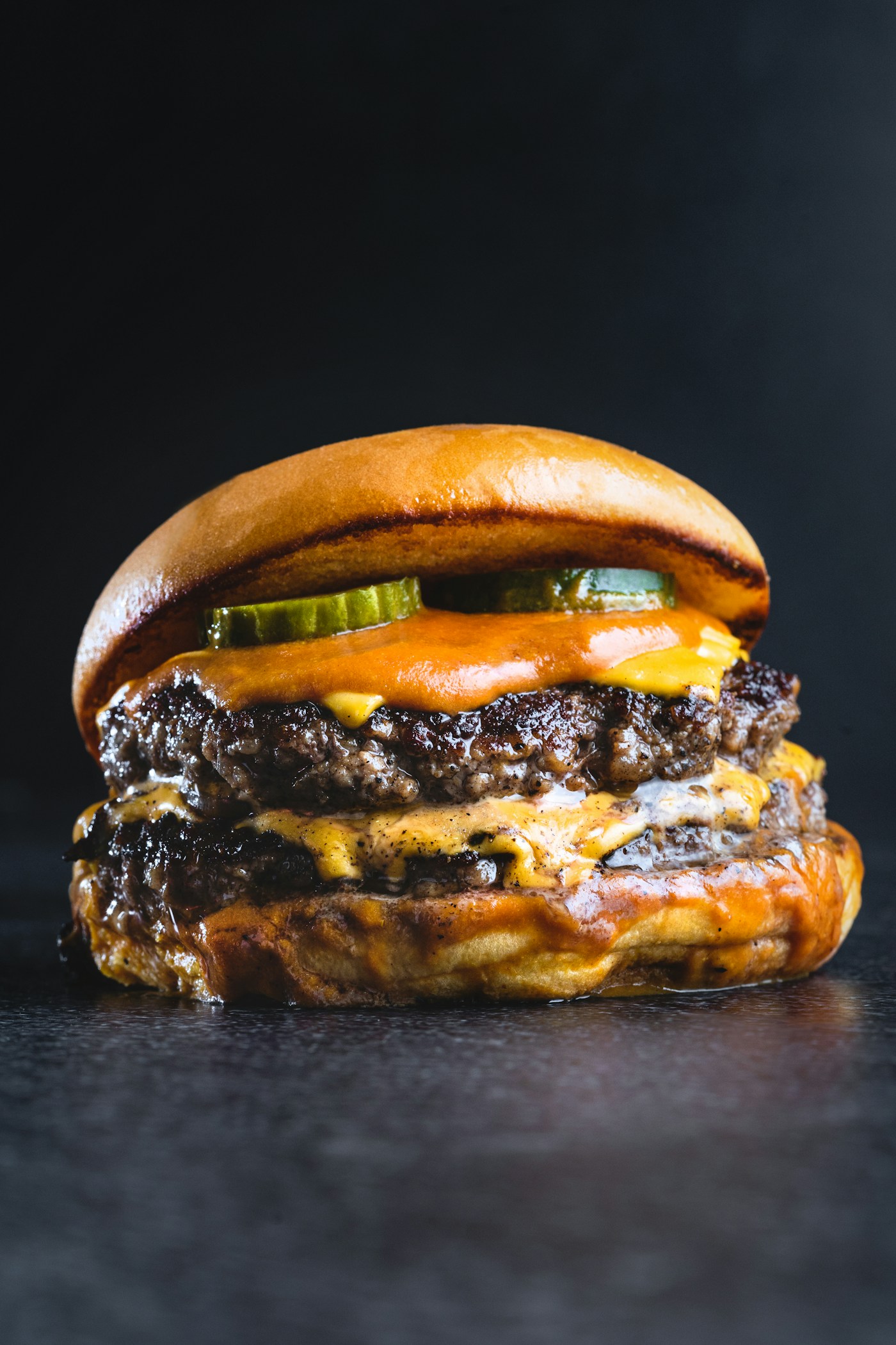 Illustrative food photograph: a double cheeseburger with pickles